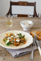 Mixed vegetable stir fry with mushrooms and cottage cream cheese. Tender mushroom stir fry served in a white plate with white wine and bread on the wooden table. Vegan food