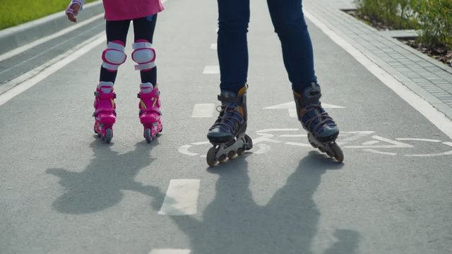 Close Up of Mother with the Daughter Go On Roller Skates Outdoors. Woman and Little Girl Rollerblading on a Bicycle Lane in a City Park. Summer Family Activities Concept