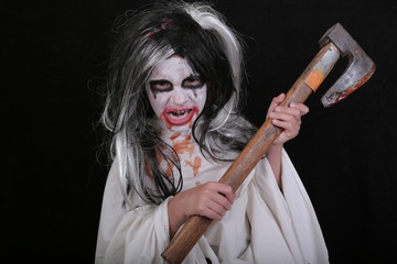 Halloween horror concept. Cute little scary girl in monster zombie costume with blood axe on black background.