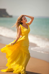 Fototapeta na wymiar young beautiful girl walks op the sandy beach in a flying yellow dress