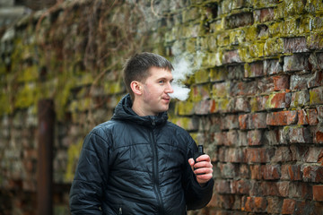 Vape man. Young caucasian white guy in black jacket smoking and letting off steam from an...