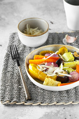 Mixed vegetable stir fry with parmesan cheese. Roasted vegetables mix on the plate with cutlery on the wicker serving mat, food above. Tender seasonal vegetables stir fry. Vegan food