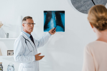 selective focus of doctor in glasses holding pen near x-ray and woman in clinic