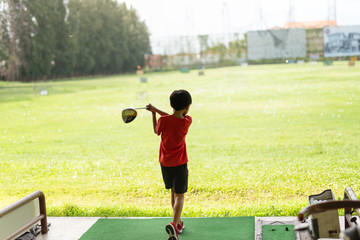 Young asian boy is practicing his golf swing at the golf driving range.