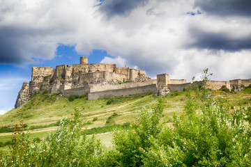 Castle ruins on a green grassy hill with dark clouds.