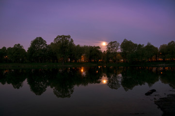 Morning sunrise on the lake in which the trees and the sun are reflected.