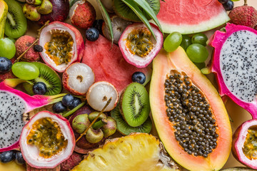 Fresh exotic fruits and tropical palm leaves on pastel orange background - papaya, mango, pineapple, passion fruit, dragon fruit, grapes, lichee, kiwi, melon. Mockup, flat lay, overhead. Top view.