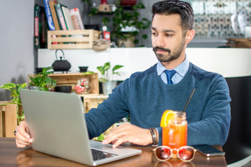 Handsome Pakistani businessman wearing smart casual clothes using laptop in a cafe