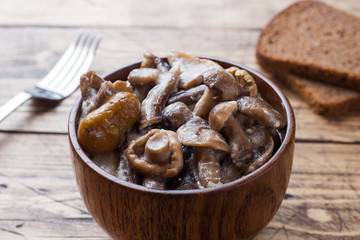 Stewed mushrooms in a sauce with sour cream and cheese in a wooden bowl.