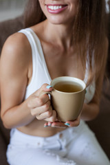 Female hands holding broun cup of tea, color manicure, smiling girl is dressed in white clothes. vertical frame