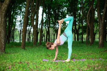 Thin brunette girl plays sports and performs beautiful and sophisticated yoga poses in a summer...