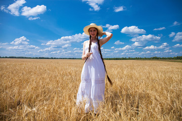 Happy brunette woman in white dress and straw hat walking in a wheat field