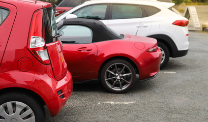 Closeup of rear, back side of red car with  other cars parking in outdoor parking area in the morning. 