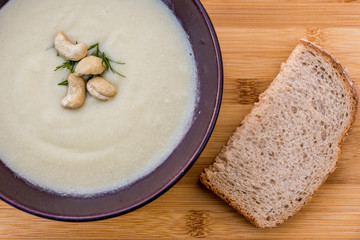 Delicious vegan cream soup with leek, potatoes, garlic and cashew nuts on wooden background with piece of bread