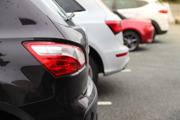 Closeup of rear, back side of black car with  other cars parking in outdoor parking area.