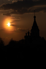Dark silhouette of a hrestian church with a bell tower against a sunset sky, flooded with orange rays of the sun