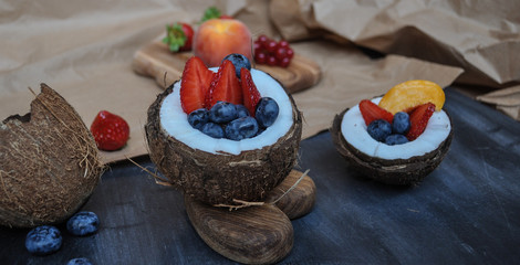 colorful fresh strawberries, blueberries and other fruits in a bowl of fresh coconut on a dark background with wood elements