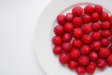 Red juicy berries. Raspberries on a white plate in a white plate isolated