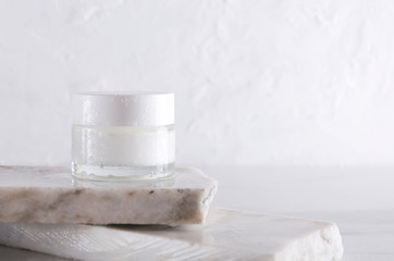 Cosmetic skincare jar on the pieces of white marble against white wall.Empty space for design