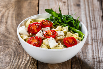 Pasta with tomatoes and white cheese on wooden table