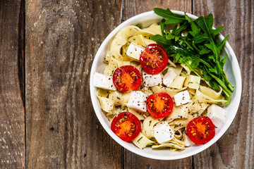 Pasta with tomatoes and white cheese on wooden table