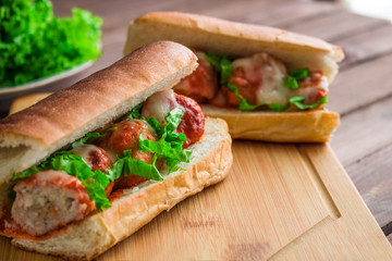homemade meatball sub sandwich halves with mozzarella and lettuce on cutting board close up