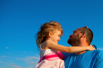 Dad is holding a happy little daughter against a bright blue sky.