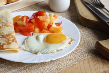 Breakfast, scrambled egg with vegetables, pancake, pepper, pastries, fork and knife on wooden board
