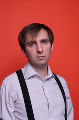 portrait of handsome confident man in pink shirt and black suspender looking at camera on orange background