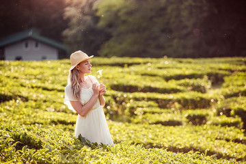 Beautiful romantic young girl in light peasant dress and a hat enjoying a walk around the tea...