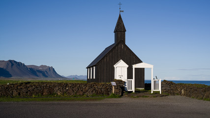 Black Church in Budir - PoI in western Iceland. The wooden church seen in late evening sun illumination slightly from the side. Its front and left side visible, ocean and mountains in background