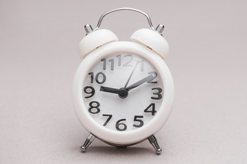 White miniature alarm clock against colored backdrop