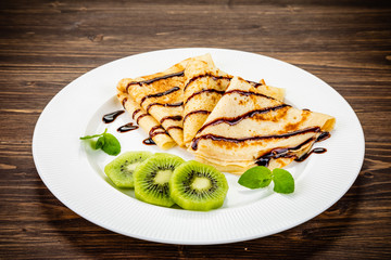 Crepes with kiwi and cream on wooden background