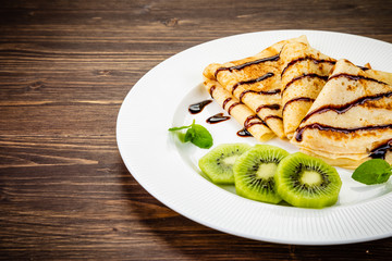 Crepes with kiwi and cream on wooden background