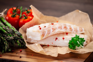 Fresh raw cod with vegetables served on cutting board on wooden table