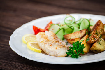 Fried fish with baked potatoes on wooden table