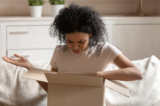 Angry african woman unpack carton box feels irritated
