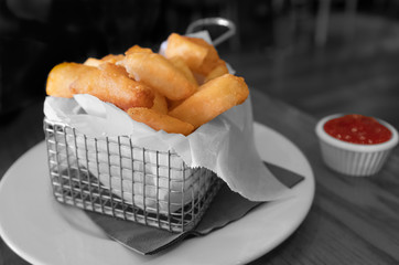 Chunky gourmet fries or chips in a square metal basket and a small tub of ketchup in selective colour with a monochrome background