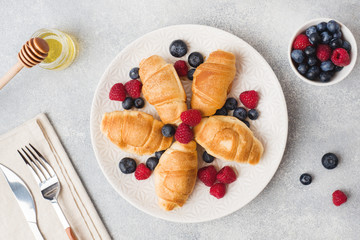 Croissants with fresh raspberries and blueberries on a dark concrete background. Copy space. concept of Breakfast coffee honey.