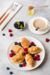 Croissants with fresh raspberries and blueberries on a dark concrete background. Copy space. concept of Breakfast coffee honey.