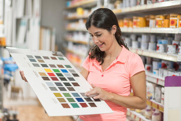 Woman with paint color swatch in specialized store looks at the different shades of color, customer...