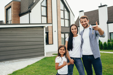 Happy heteroseksual family standing near their new house. Man holding keys from new apartment.