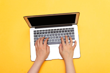 women typing on keyboard of modern laptop isolated on yellow background