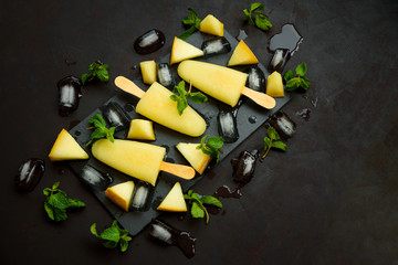 Homemade melon ice cream, pops or popsicles with ice, melon slices and mint on rectangular dark slate plate. Summer food. Flat lay. Top view