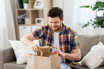 consumption, eating and people concept - smiling man unpacking takeaway food at home