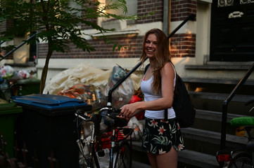 Fototapeta na wymiar Happy Dutch student girl with her bicycle in front of her student house which has a lot of plastic garbage outside 