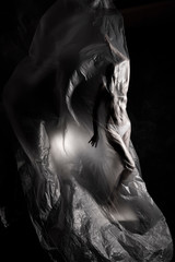 Slim girl dressed only in underwear emotionally posing, wrapped in fluttering in the wind and fitting her graceful young body cellophane film. Artistic, creative, abstract design. Black and white