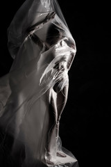 Slim girl dressed only in underwear emotionally posing, wrapped in fluttering in the wind and fitting her graceful young body cellophane film. Artistic, creative, abstract design. Black and white