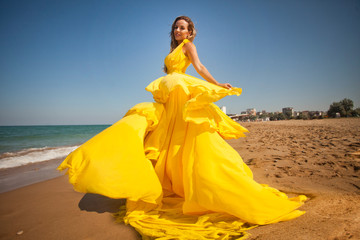 young beautiful girl walks op the sandy beach in a flying yellow dress