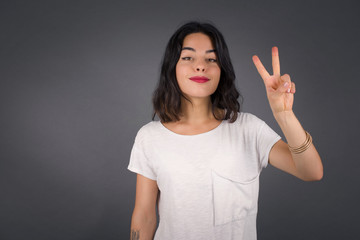 Young middle aged caucasian woman standing against gray wall showing and pointing up with fingers number two while smiling confident and happy.